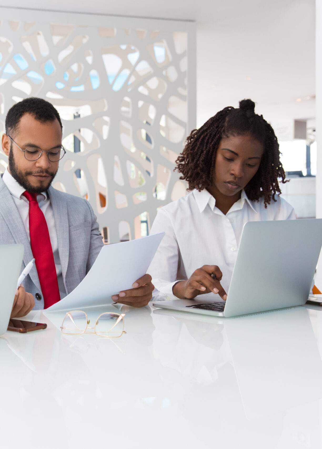 Business professionals checking project data together. Business man and women sitting at conference table, using laptops, reading documents. Working professionals concept